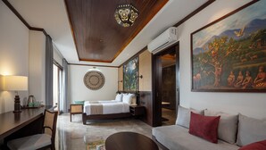 A hotel room with a bed, a sofa, a desk, and a painting on the wall. - Emana Abian Taksu (Payangan)