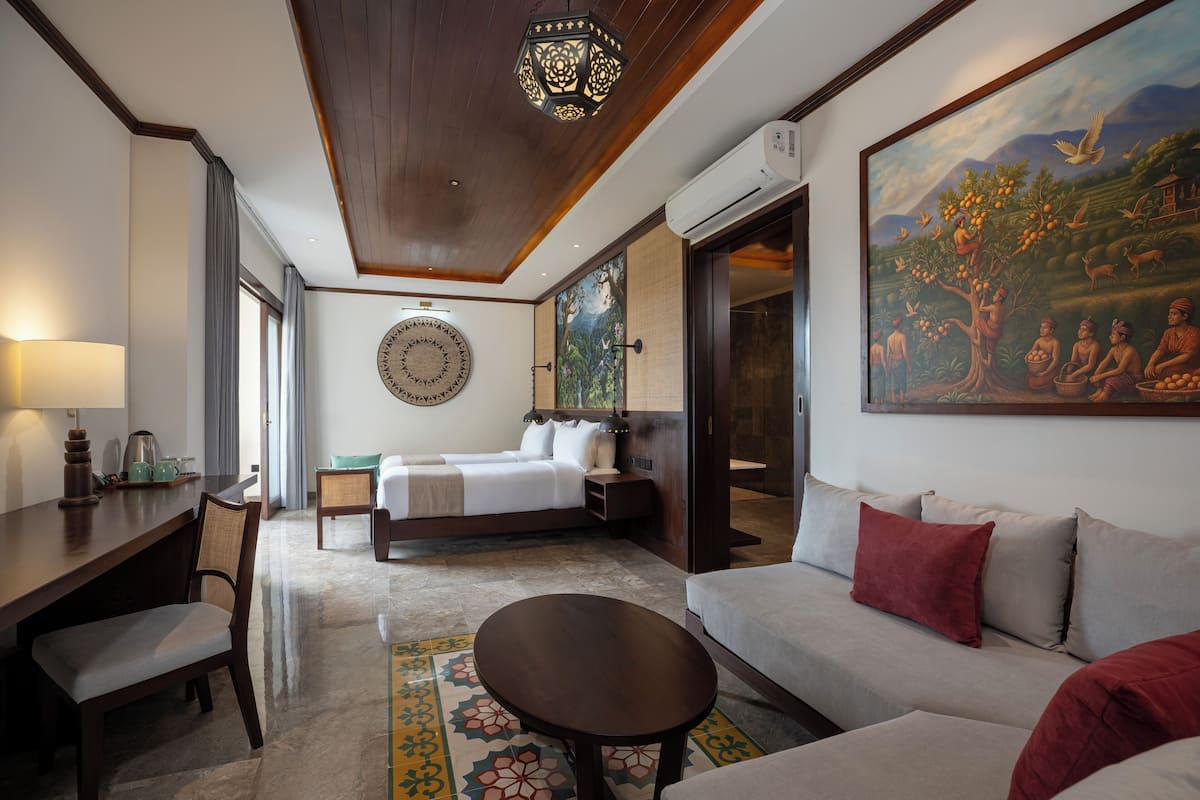 A hotel room with a bed, a sofa, a desk, and a painting on the wall.