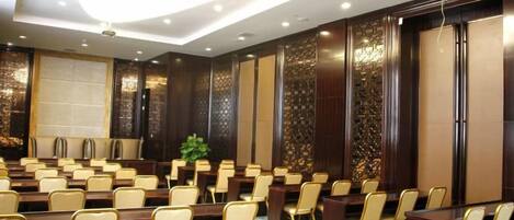 A conference room with rows of tables and chairs, a large plant, and decorative wall panels.