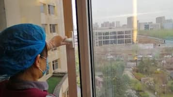 A person in a blue head covering and a red vest standing by a window, looking outside.