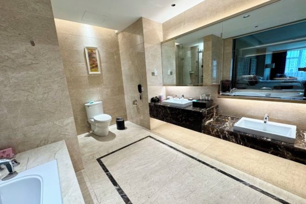 A modern bathroom with a large mirror, a bathtub, a toilet, and a sink.