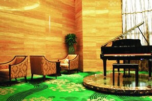 A grand piano in a room with a patterned carpet, a large potted plant, and a wall with a wooden finish. - Yushui Hotel (Shahe)