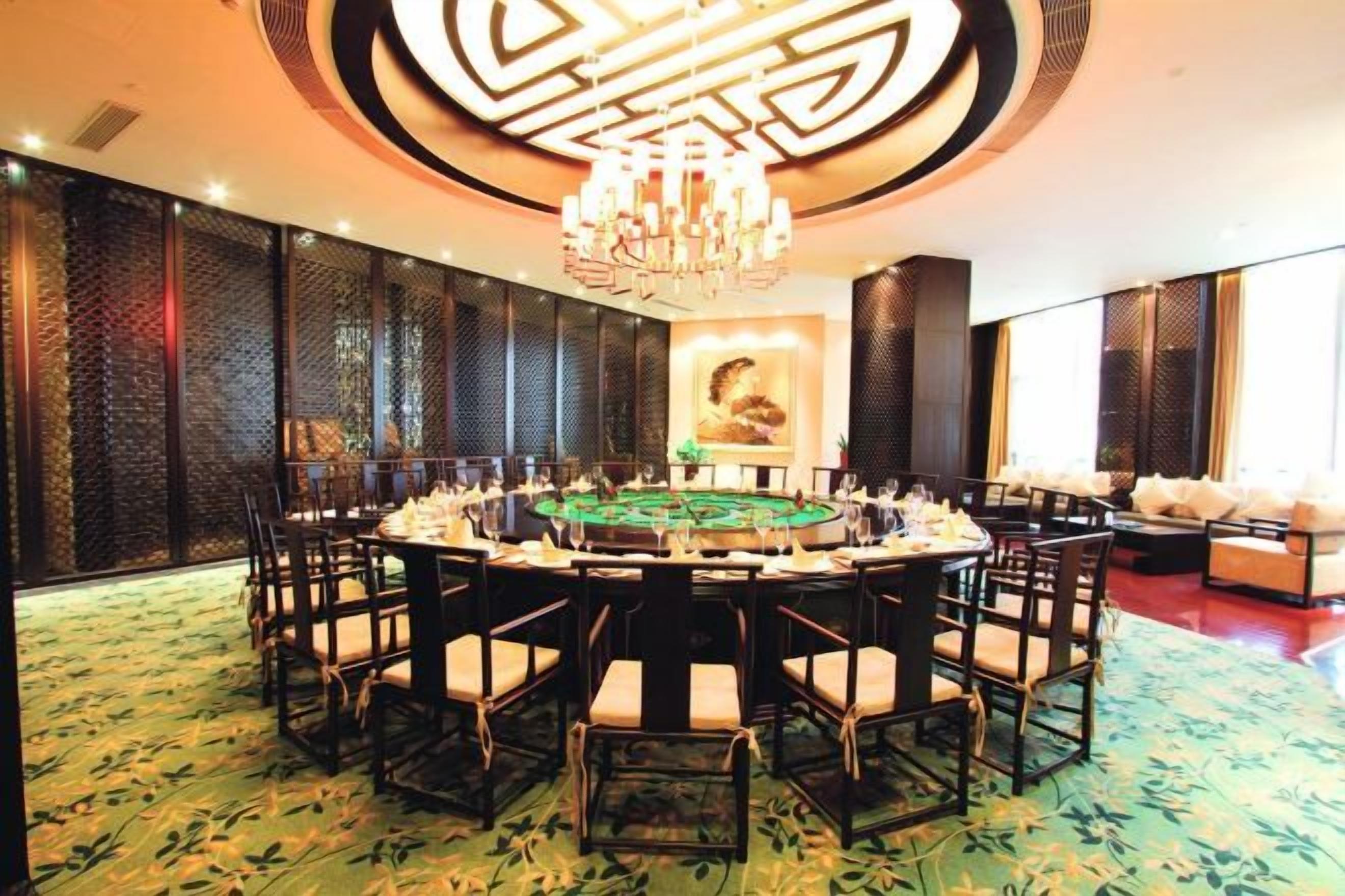 A round table with chairs arranged around it, a chandelier above, and a patterned carpet.