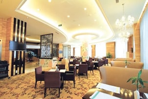 Un hall de hotel con una zona de estar central, un mostrador de recepción y una escalera que conduce a los pisos superiores.