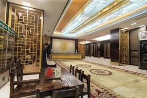 A hotel lobby with a reception desk, seating area, and a decorative wall with a circular emblem.