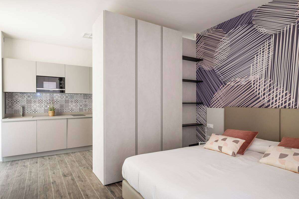 A modern bedroom with a large bed, a built-in wardrobe, and a kitchen area with a microwave.