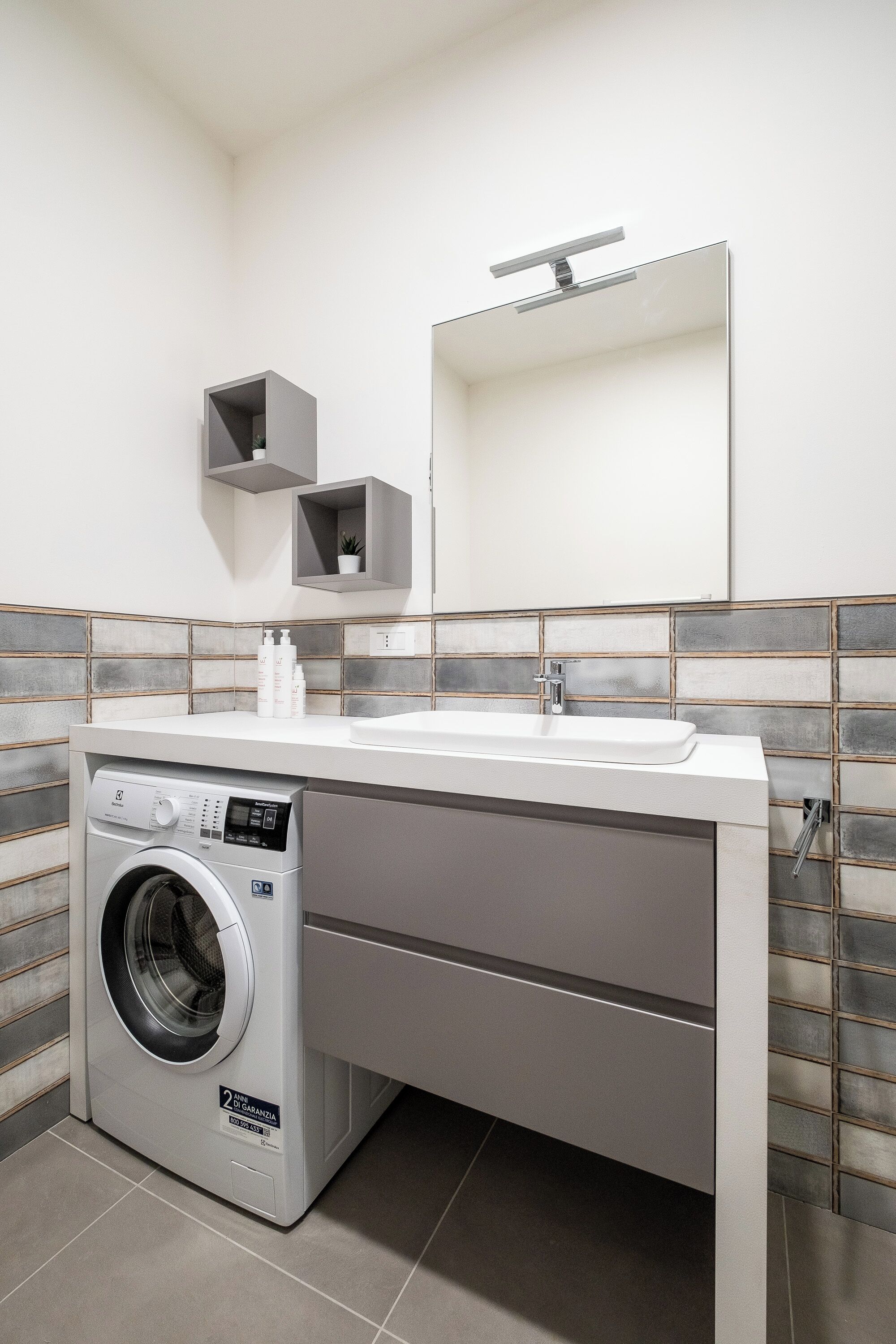 A modern laundry room with a built-in washing machine, a sink, and a mirror.