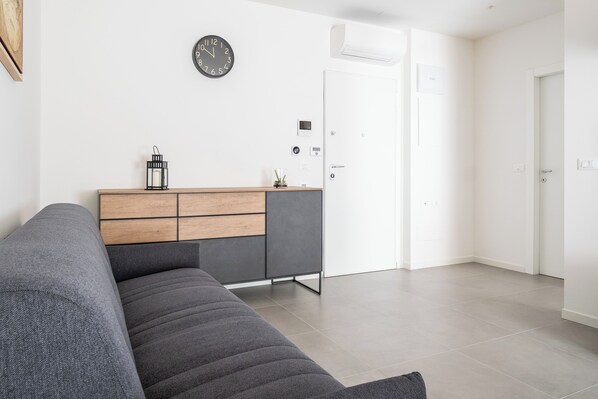 A modern living room with a grey sofa, a wooden cabinet, and a wall clock. - Appartamenti Ariosti a un Passo da Piazza Maggiore by Wonderful Italy (Bologna)