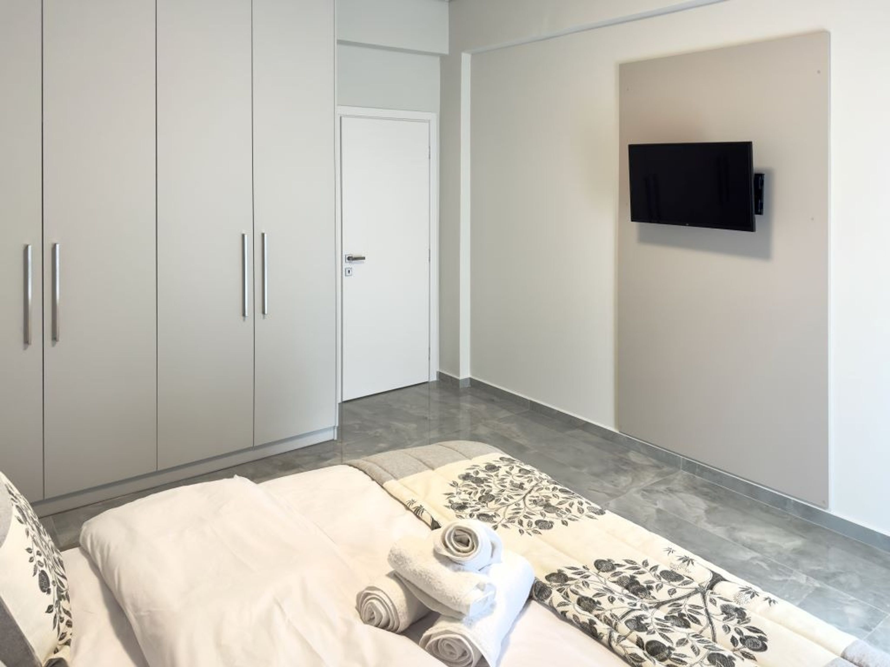 Un dormitorio con cama, armario y televisor montado en la pared.