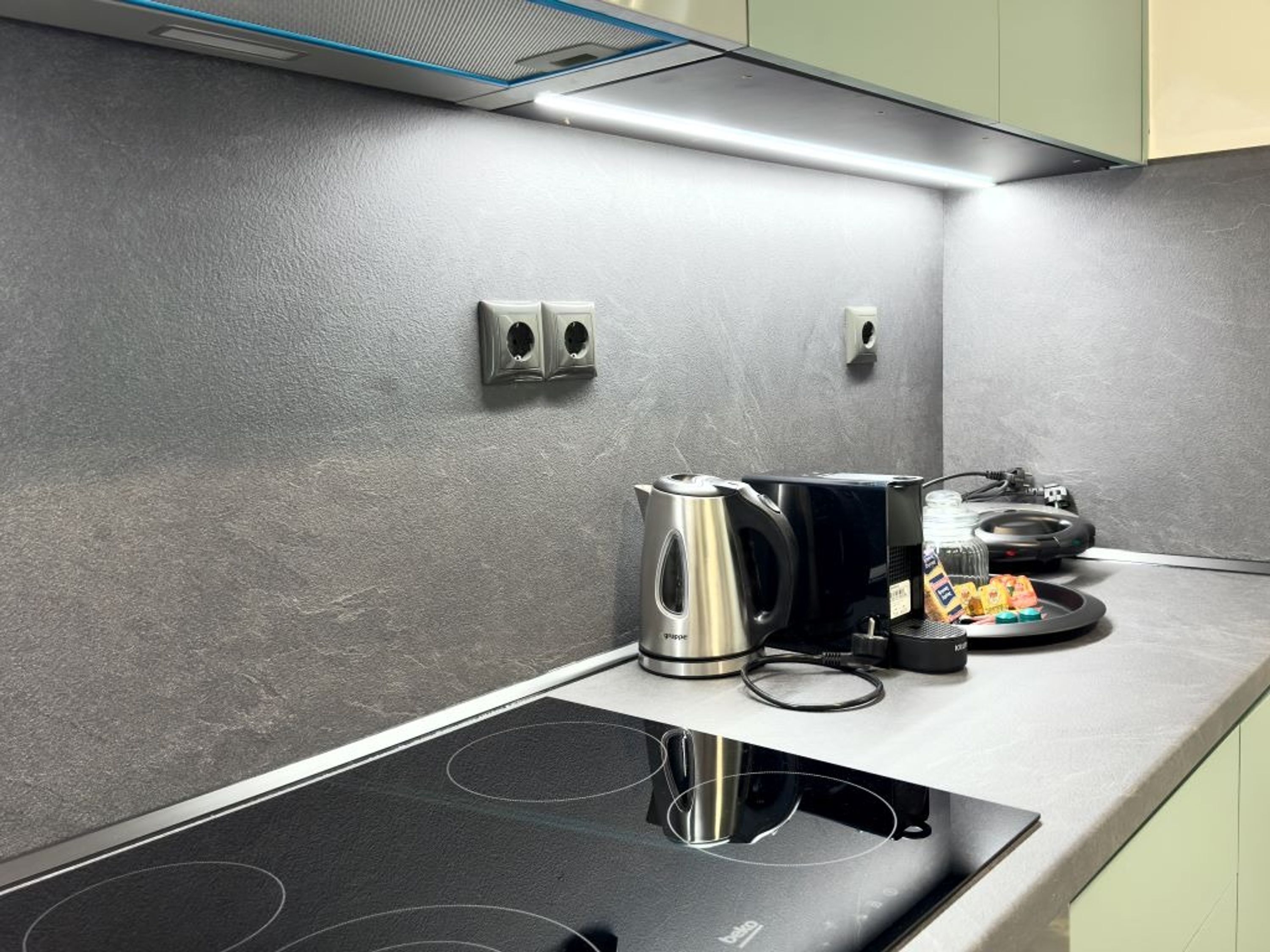 A modern kitchen with a black induction cooktop, a stainless steel kettle, and a coffee maker.