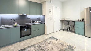A modern kitchen with teal cabinets, stainless steel appliances, and a patterned rug. - City Bliss I Trikala Town (Trikala)