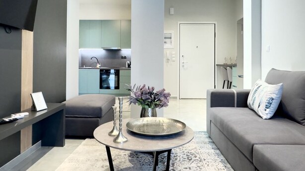 A modern living room with a grey sofa, a round coffee table, and a flat-screen TV mounted on the wall. - City Bliss I Trikala Town (Trikala)