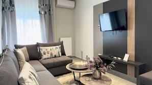 A modern living room with a grey sofa, a round coffee table, and a flat-screen TV mounted on the wall. - City Bliss I Trikala Town (Trikala)