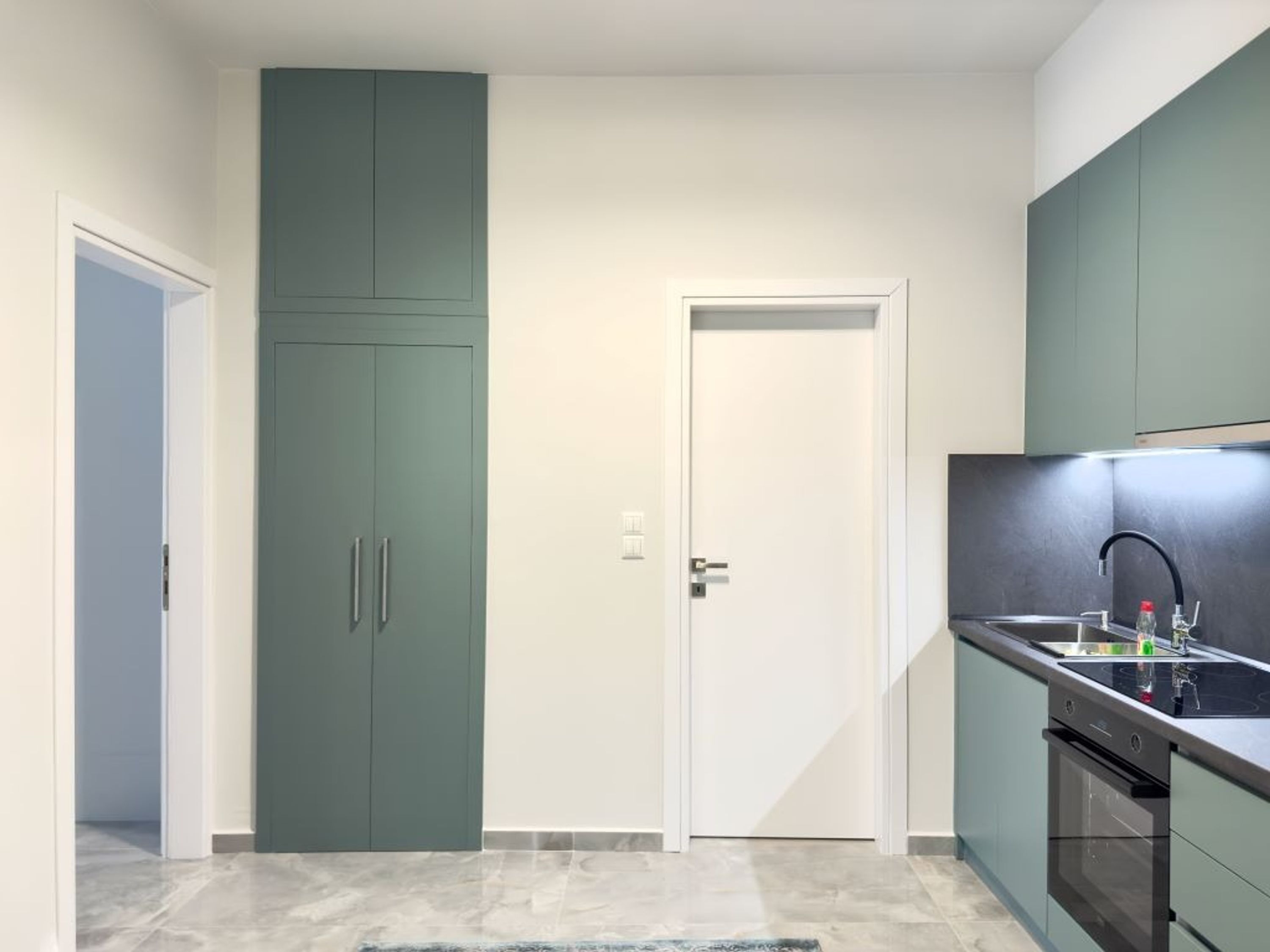 Una cocina moderna con armarios verde azulado, una puerta blanca y una encimera negra con un lavabo y una estufa.