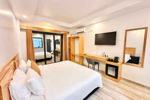 Hotellihuone, jossa on suuri sänky, työpöytä tuolilla, seinälle asennettu televisio ja peili.