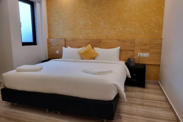 A modern hotel room with a large bed, a wooden headboard, and a small bedside table with a lamp.