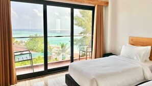 A hotel room with a large window offering a view of the ocean and a distant building. - AIMI Beach, Gulhi Island, Maldives (Gulhi)