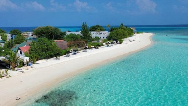 A beach with clear turquoise water, white sand, and a row of buildings along the shore. - AIMI Beach, Gulhi Island, Maldives (Gulhi)