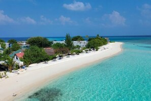 A beach with clear turquoise water, white sand, and a row of buildings along the shore.