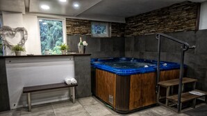 Une salle de bain moderne avec une baignoire en bois, un banc, une décoration en forme de cœur et une fenêtre donnant sur un paysage verdoyant.