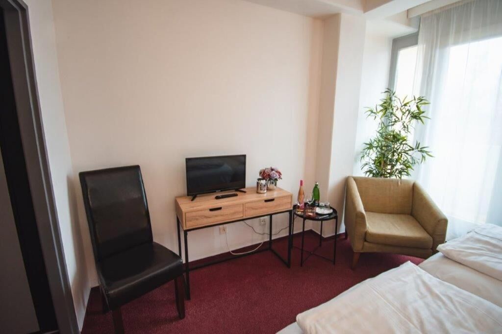 Hotelkamer met een bed, een bureau met televisie, een stoel, een kleine tafel met een plant en een raam met gordijnen.