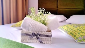 Cama bem arrumada com lençóis brancos, manta verde e cesta decorativa com laço xadrez.