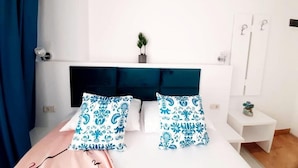 Quarto com cama, cabeceira, mesa de cabeceira, uma pequena planta e um espelho.