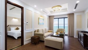 A hotel room with a bed, a sofa, an ottoman, a coffee table, and a view of the sea. - Victory Hotel Vung Tau - New Wing (Vung Tau)