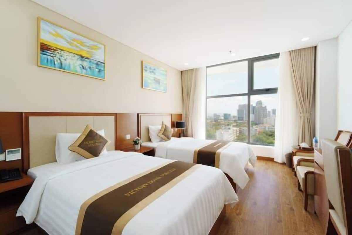 Camera d'albergo con due letti, una grande finestra vista città e un quadro appeso al muro.