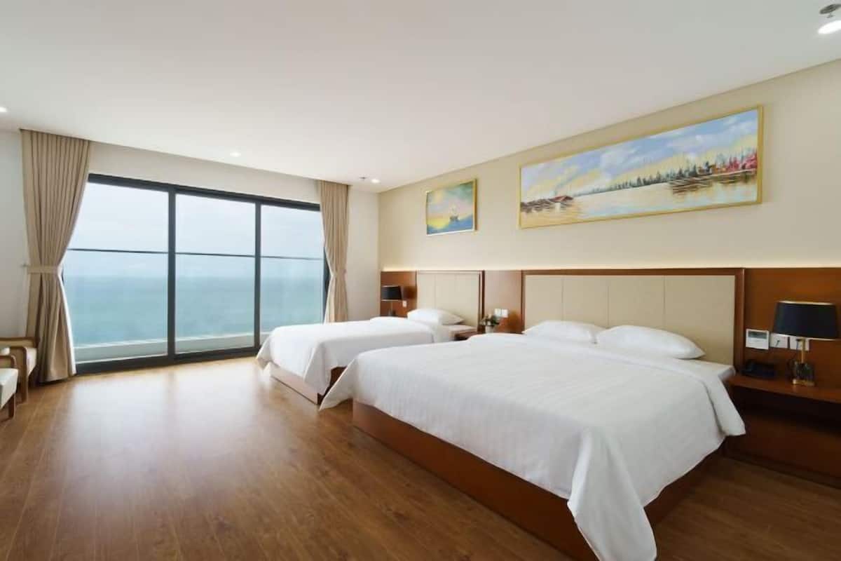 Una camera d'albergo con due letti, una grande finestra vista e due quadri appesi al muro.