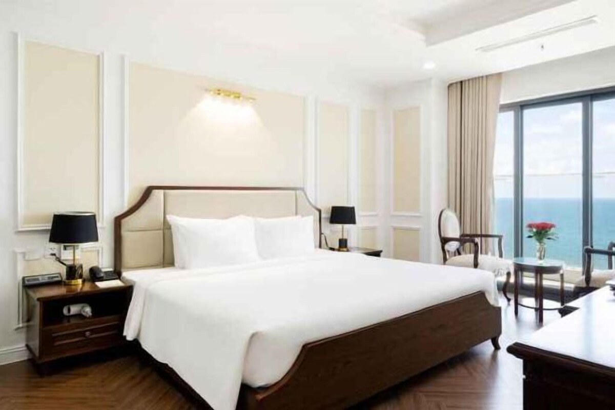 Une chambre d’hôtel avec un grand lit, des tables de chevet, une chaise et une vue sur la mer.
