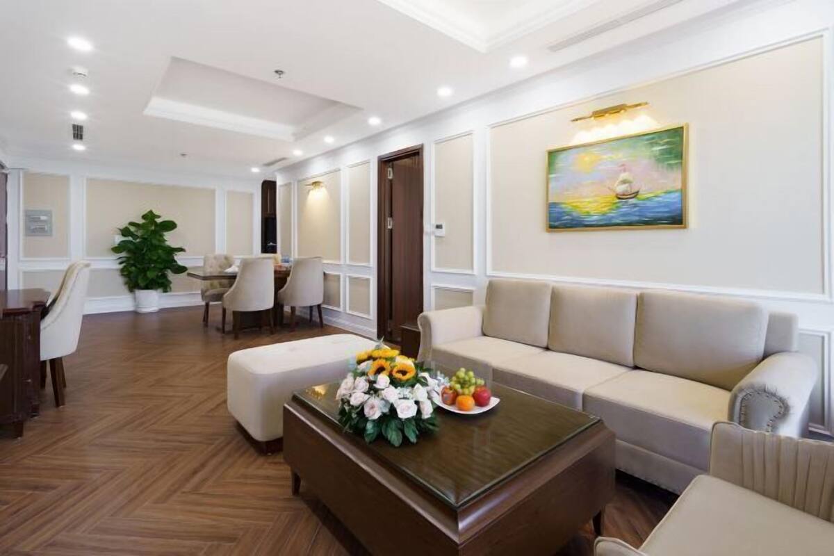 Una hall d'albergo con una poltrona, sedie, un tavolino da caffè con fiori, un quadro e una pianta in vaso.
