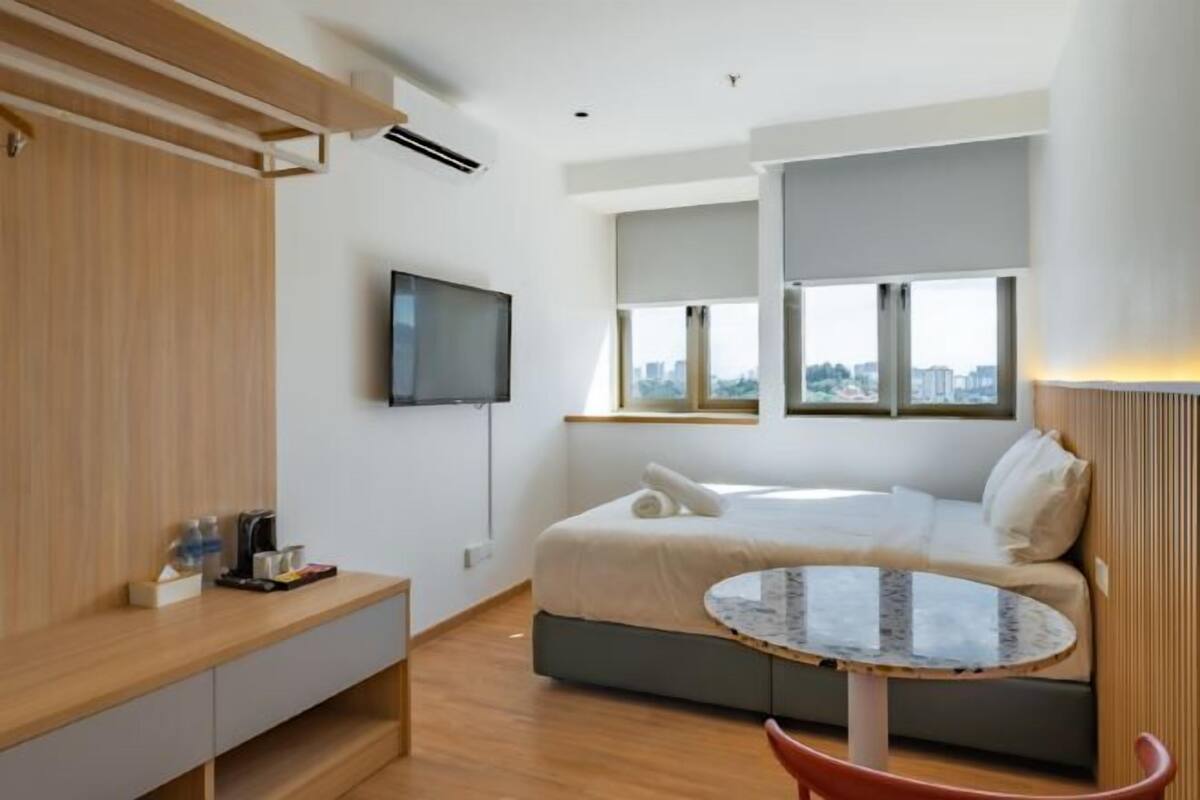 A modern hotel room with a bed, a TV, a small round table, and a window with a city view.