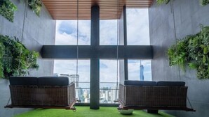 Un intérieur moderne avec deux fauteuils suspendus en osier, un plafond en bois et une grande fenêtre donnant sur la ville.