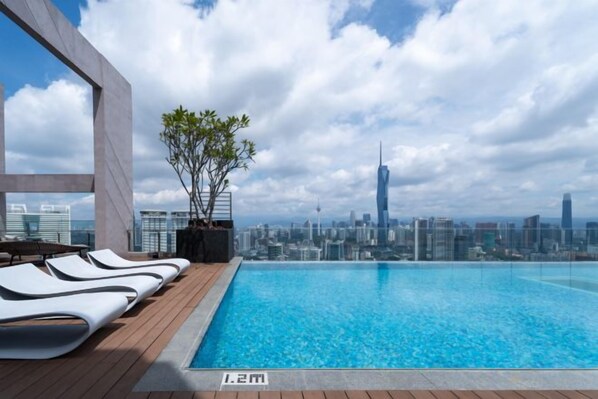 An infinity pool with a city skyline view, lounge chairs, and a wooden deck. - Upper Suites Kl Sentral (Kuala Lumpur)