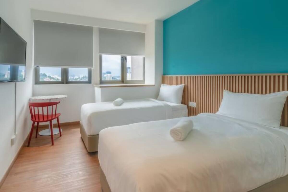 A hotel room with two beds, a red chair, a small table, and a city view.