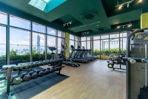 Une salle de sport équipée de matériel d’exercice, dotée de grandes fenêtres et offrant une vue sur la ville.