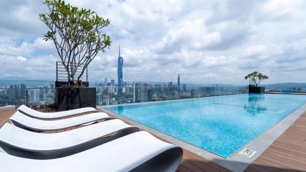 Une piscine à débordement située sur le toit, avec des chaises longues, un pot de fleurs et une vue panoramique sur la ville.