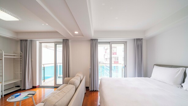 Habitación de hotel con una cama grande, un sofá, una mesita y un balcón con cortinas.