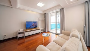 Un moderno salón con un televisor de pantalla plana, un sofá blanco, una mesita de centro y un balcón con vistas.