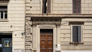 A building facade with a central entrance featuring a double wooden door, flanked by stone and brick elements, and two windows with shutters.