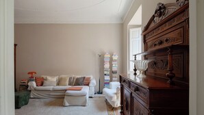 A living room with a sofa, ottoman, and a wooden cabinet. There are bookshelves with books and a lamp on the cabinet.