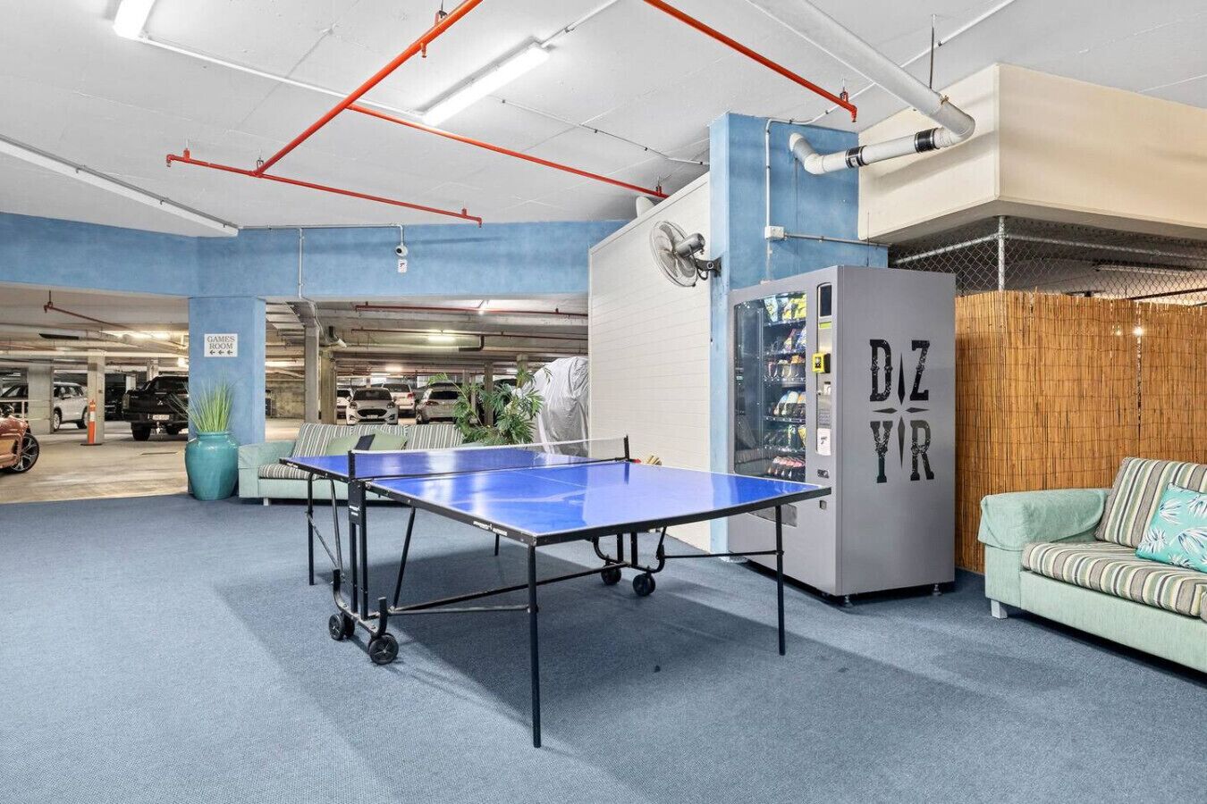 A ping pong table in a modern indoor space with a blue wall, a vending machine, and a green sofa.