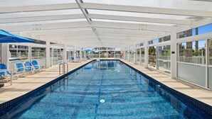 A covered swimming pool with blue tiles, sun loungers, and glass doors leading to outdoor areas. - Lookout Palm Beach - Absolute Beachfront + Views (Palm Beach)