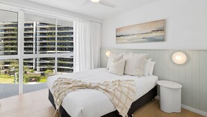 A bedroom with a bed, a ceiling fan, a bedside table, and a large window with curtains. - Lookout Palm Beach - Absolute Beachfront + Views (Palm Beach)