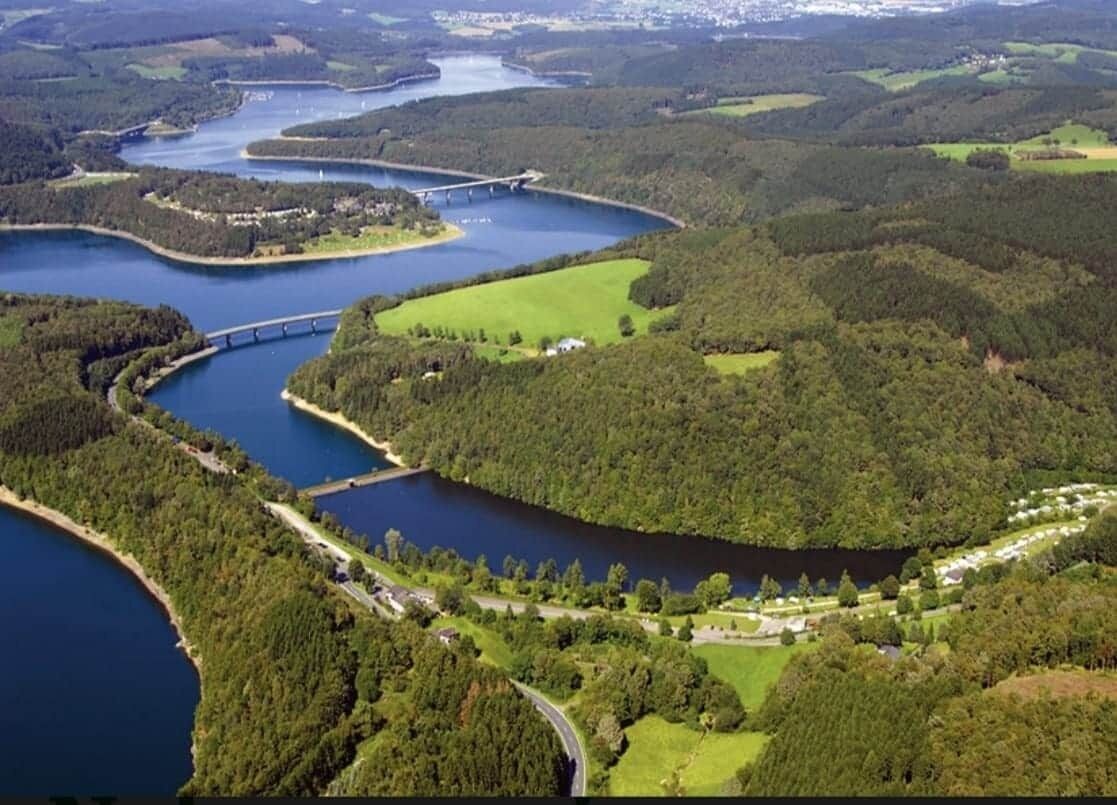 An aerial view of a lake surrounded by forested areas and a bridge.