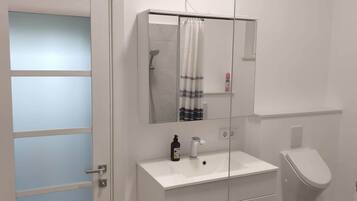Een moderne badkamer met een wit wastafelmeubel, een douchecabine met glazen wanden en een toilet.