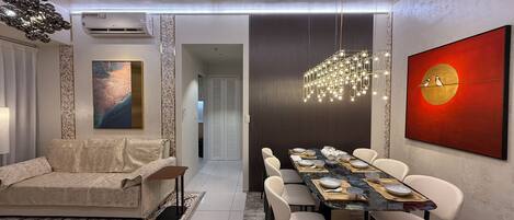 A modern dining area with a long table set for six, surrounded by white chairs.