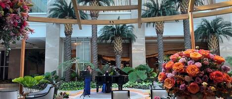 A spacious atrium with a central stage, palm trees, and a large floral arrangement.