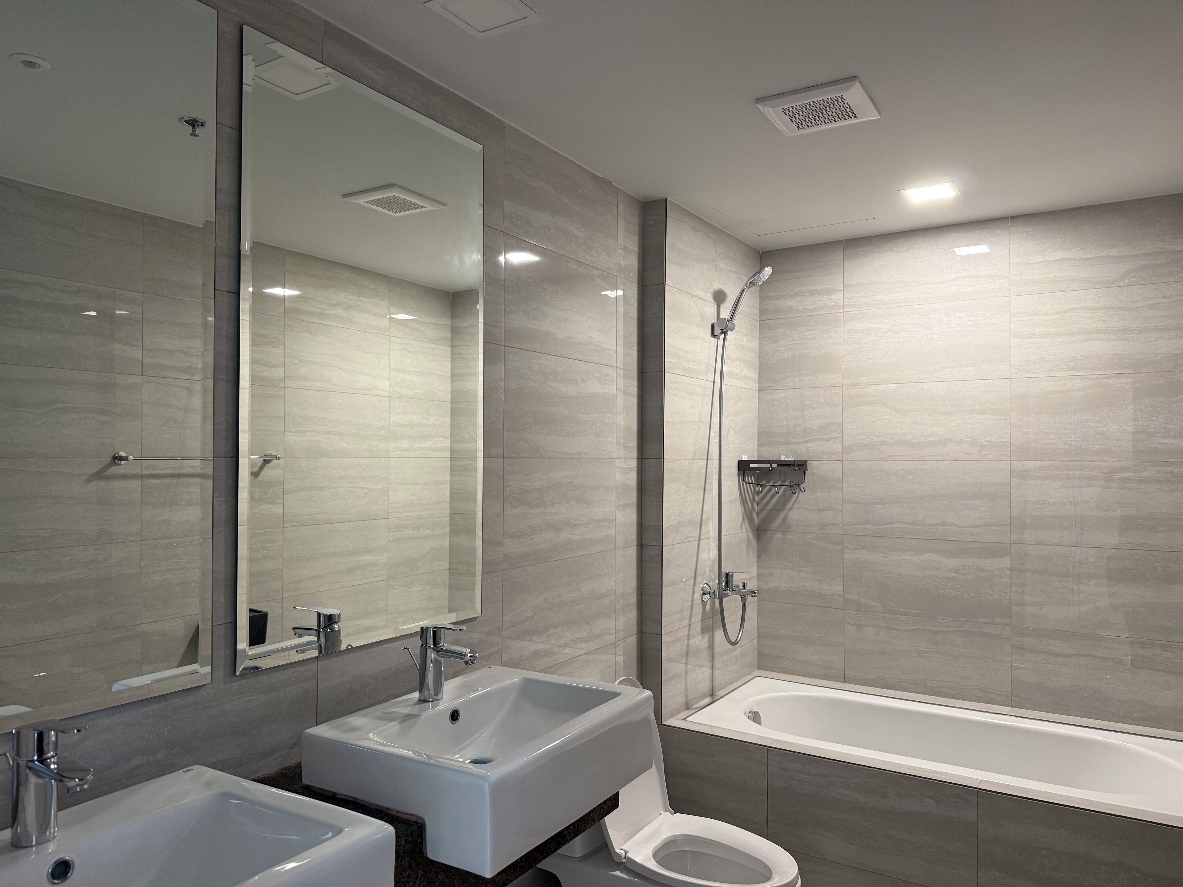 A modern bathroom with a large mirror, two sinks, a toilet, and a bathtub.